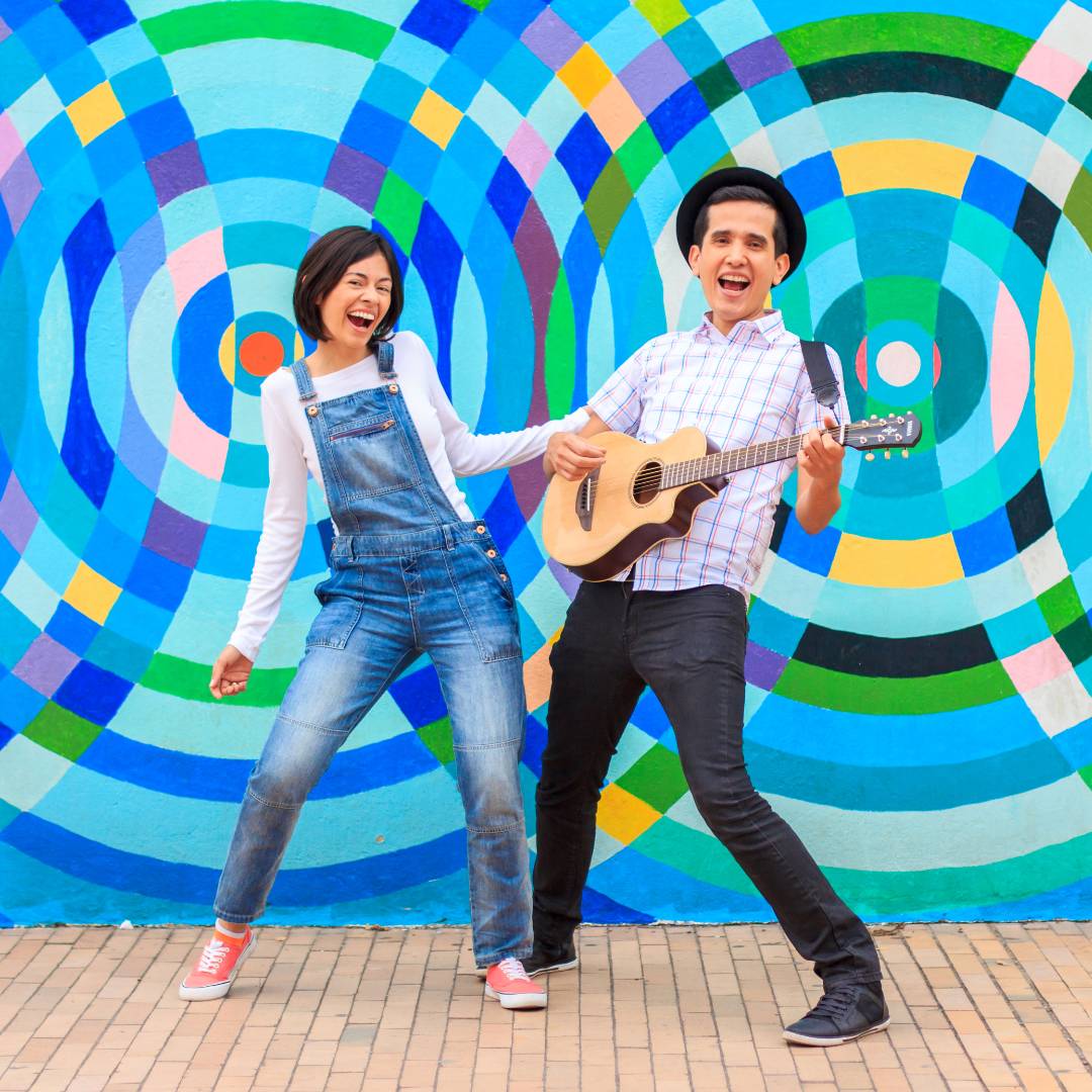 Two people smiling with a guitar and a vibrant background 
