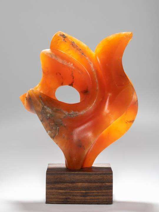 Abstract orange sculpture with flowing curves on a wooden base