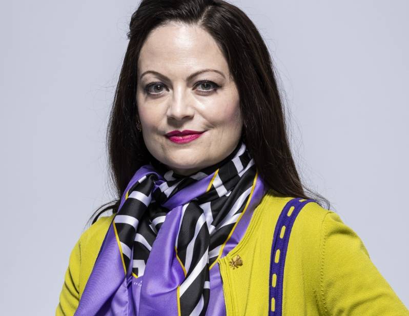 Dean of the School of the Arts, Courtney Davis Woman wearing a yellow cardigan and mulicolored scarf against a gray background