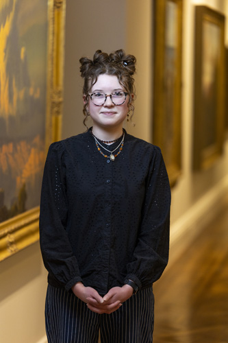 A person standing in an art gallery with paintings on the walls.              