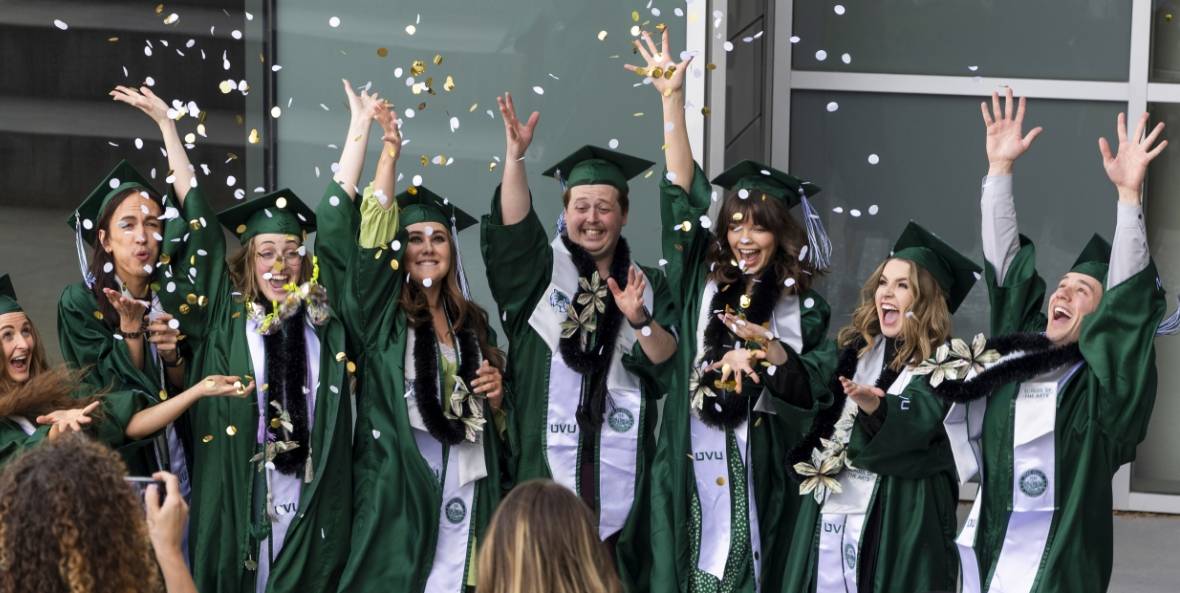 Graduation A group of graduates in green caps and gowns celebrating by tossing confetti in the air