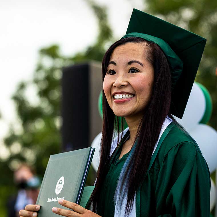 Student in green cap and gown receives degree at convocation.