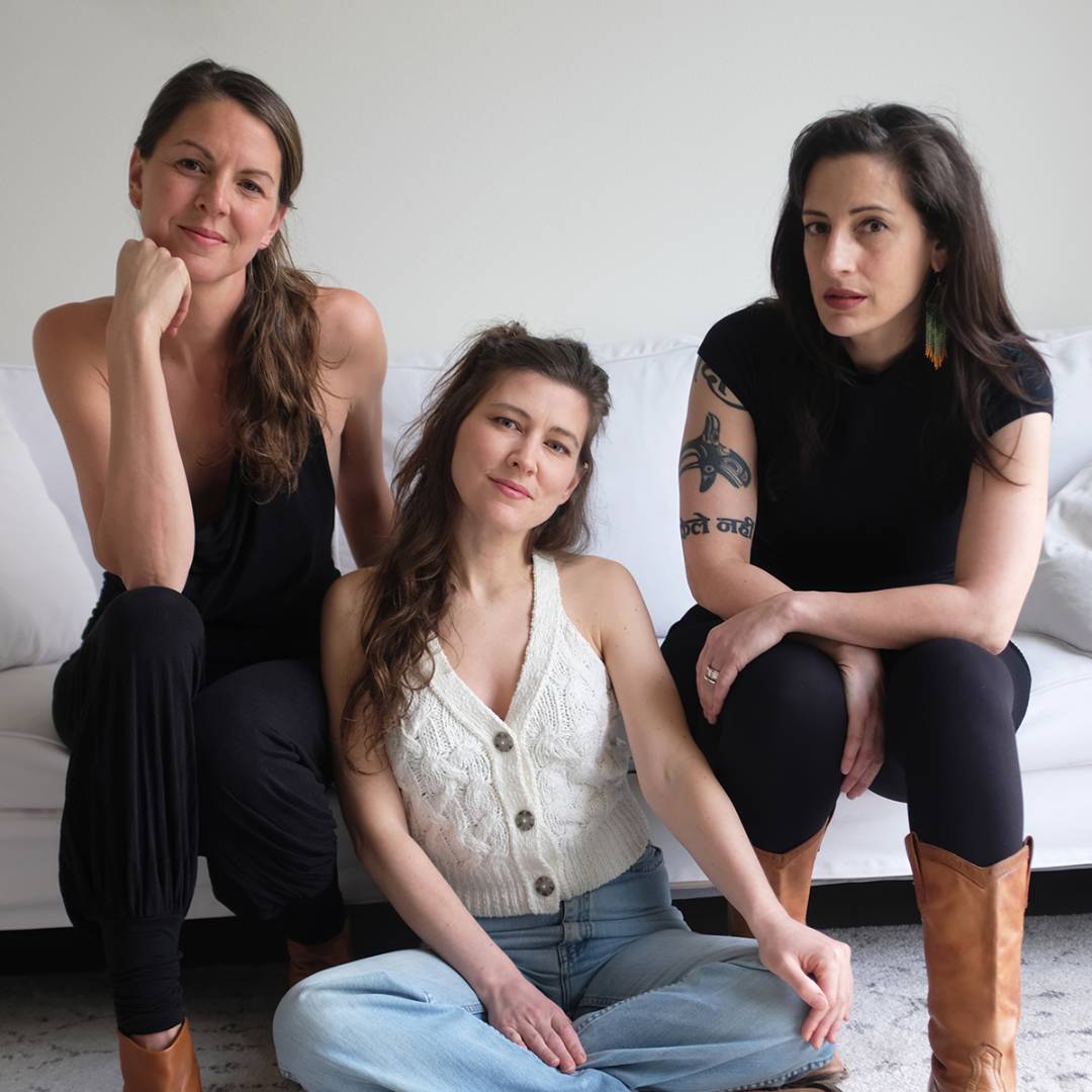 Three women seated on a white sofa, facing the camera.              