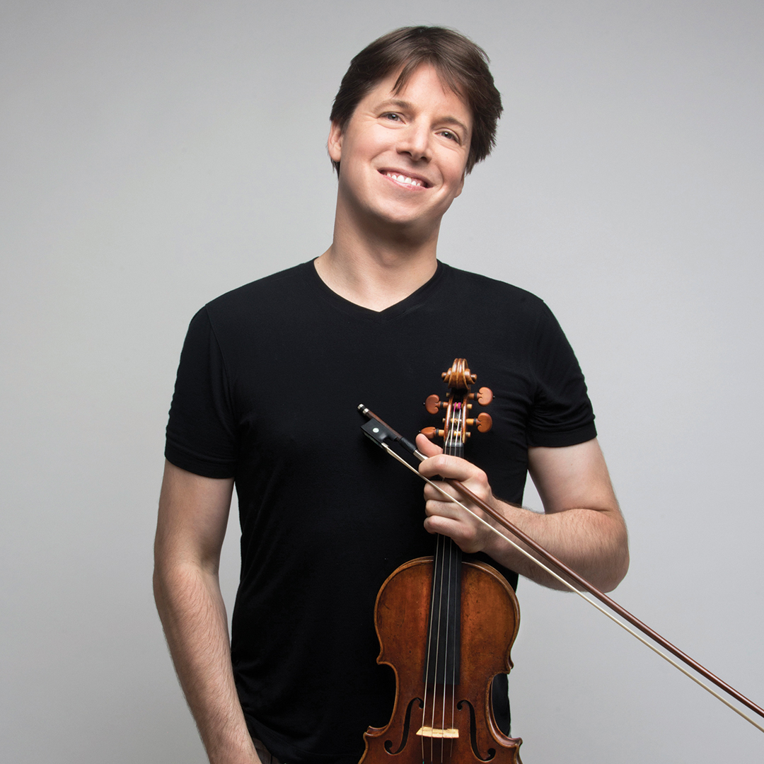 A person playing the violin with a focused expression on a dimly lit stage.