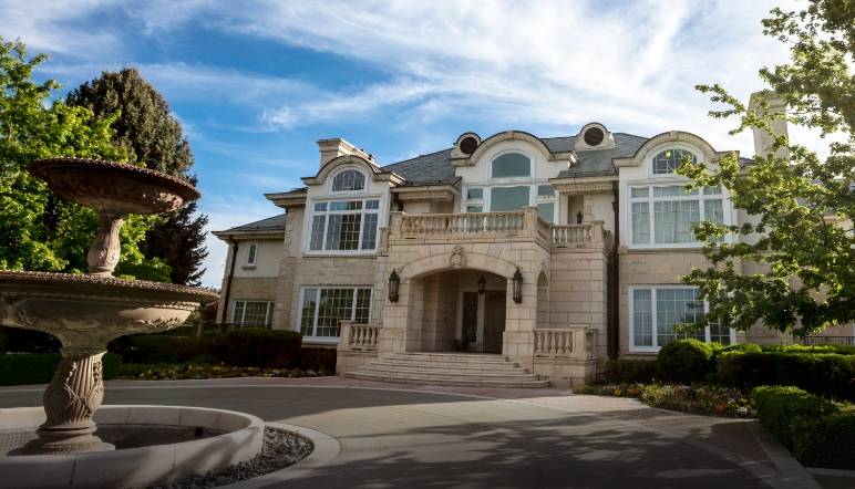 Large two-story house with light stone facades and a circular driveway with a fountain