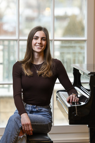 Young woman sitting at a piano in front of a large window.              