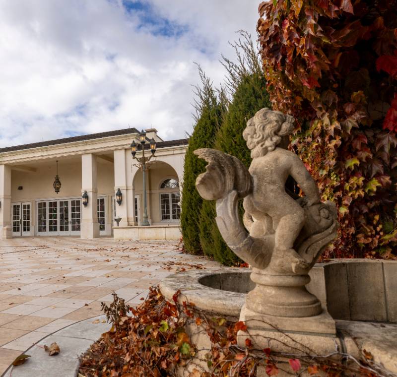 A classical building with columns and a cherub statue fountain, surrounded by autumn ivy.              