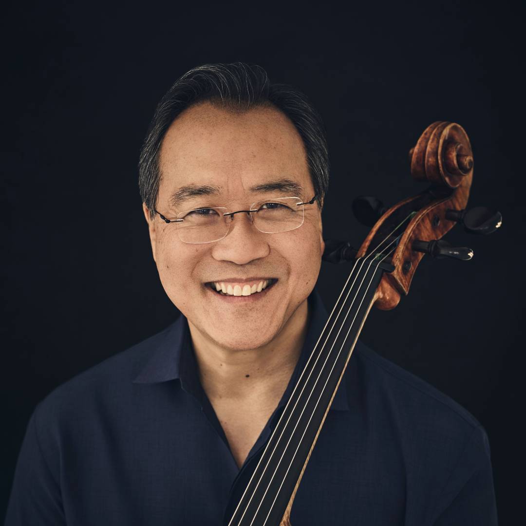 Person smiling with a cello against a dark background.              