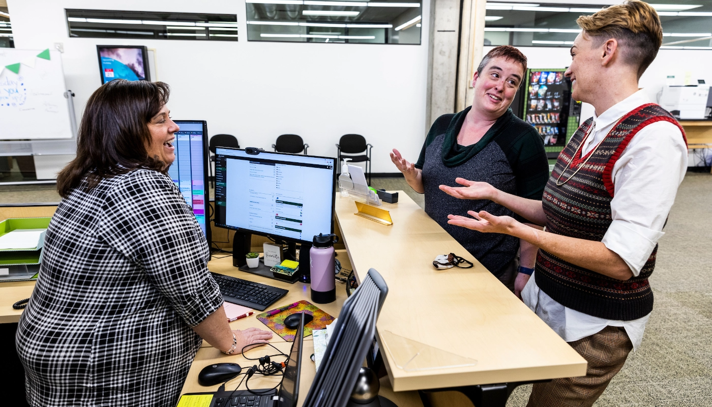 Three employees standing around a desk having an animated conversation.