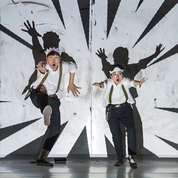 Two performers in motion against a black and white radial backdrop, striking dynamic poses.