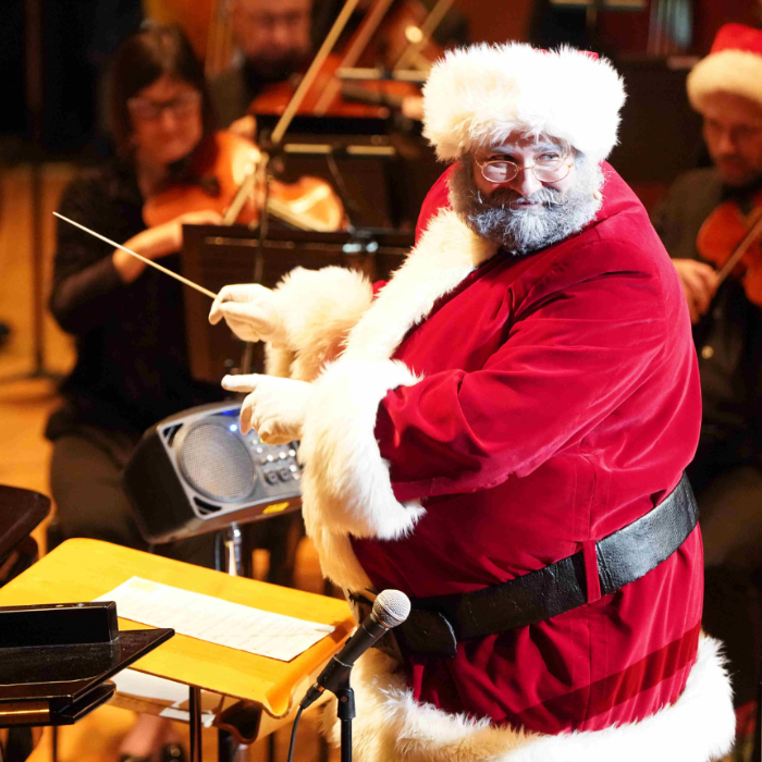 Person in a Santa Claus costume conducting an orchestra.              
