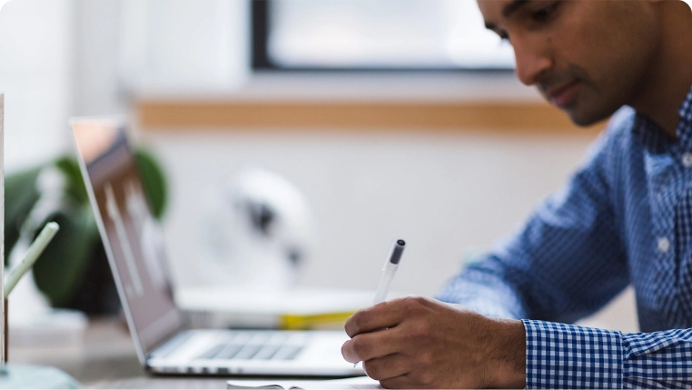 Man sitting in front of a laptop computer, writing on paper next to the computer.