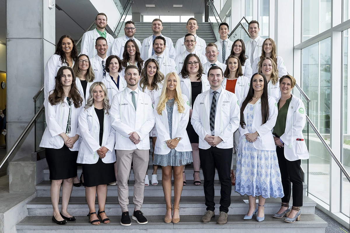The first graduating cohort from UVU’s physician assistant program smile while wearing white coats on UVU campus. 