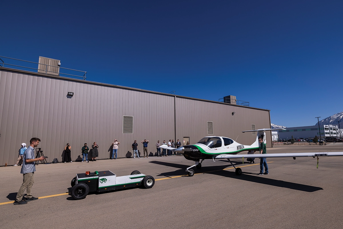 Mechanical engineering and computer science students stand on an airfield while showing the operation of an autonomous electric airplane tug, which bears UVU’s logo. 