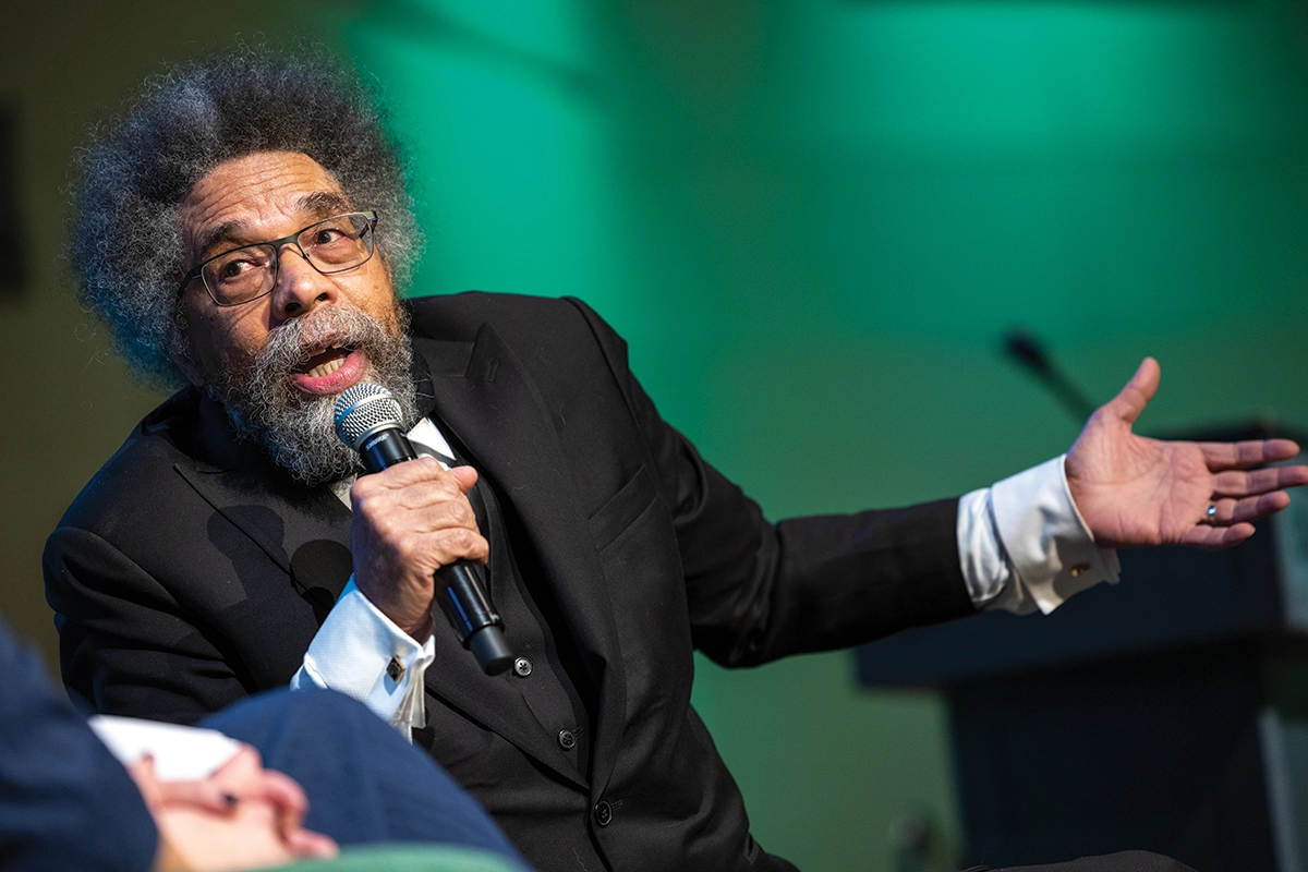 Political activist Dr. Cornel West, wearing a black suit, speaks into a microphone on UVU campus. 