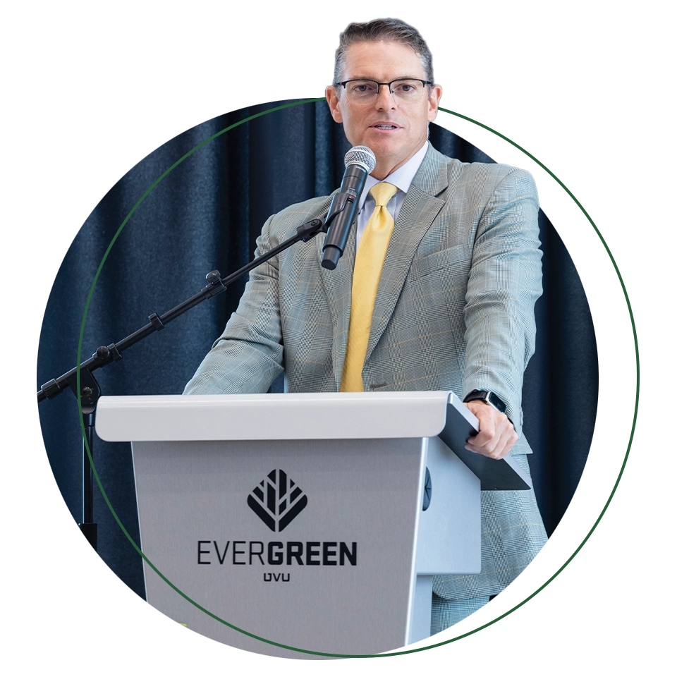 Utah Valley Chamber of Commerce President and CEO Curtis Blair, wearing a gray suit and yellow tie, speaks at a podium. 